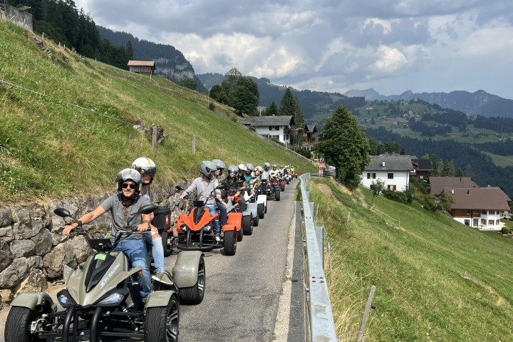 Group of people riding quad bikes on a narrow road in a mountainous area.