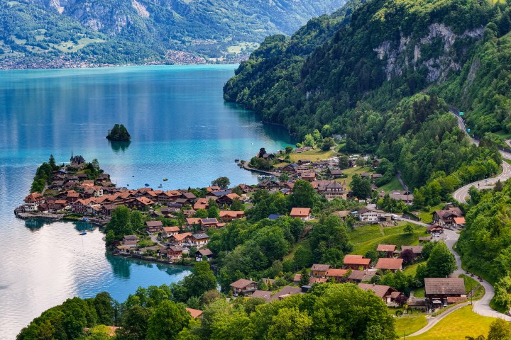 Aerial view of a lakeside village with red-roofed houses surrounded by green mountains.