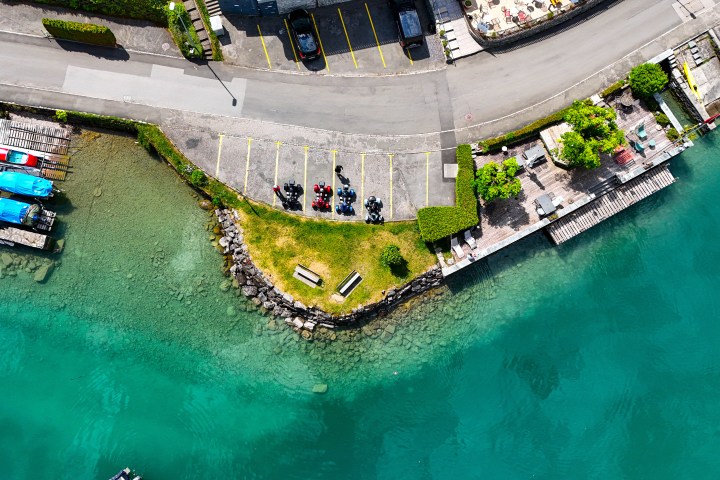Aerial view of a coastal parking area with parked motorcycles by clear turquoise water.