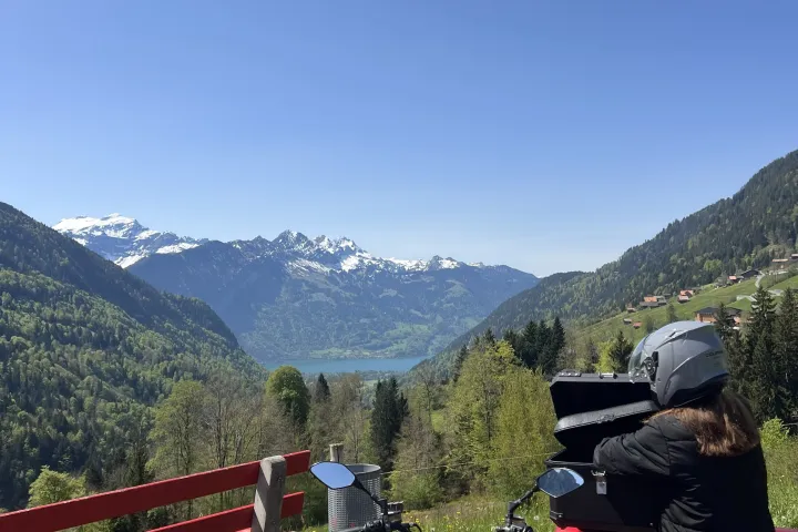 Person on red motorcycle overlooking mountains and lake under clear blue sky.