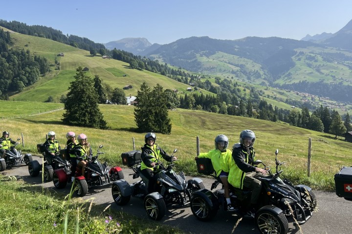 Group of people riding three-wheeled vehicles on a scenic mountain road.