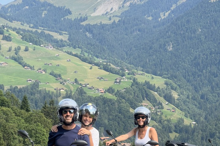 Three people on quad bikes in front of a mountain landscape.