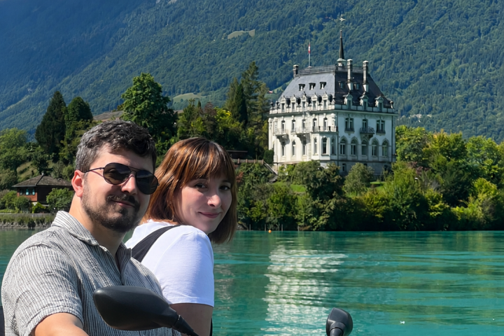 Two people on a jet ski with a scenic mountain and lake backdrop.